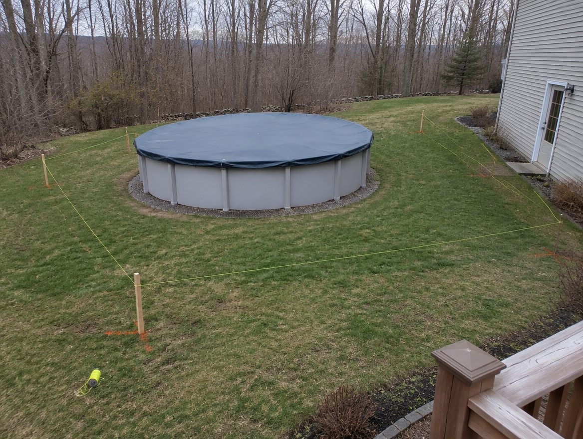 An above-ground pool with a fence line staked out on three sides and the house wall on the fourth