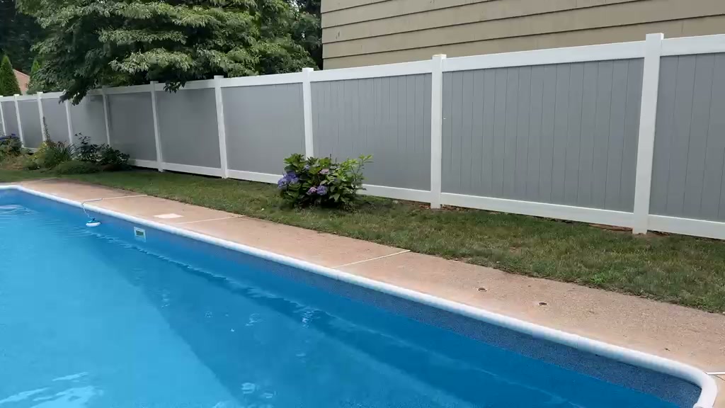 Gray vinyl privacy fence panels with white posts and rails running beside a pool deck with hydrangeas at the base