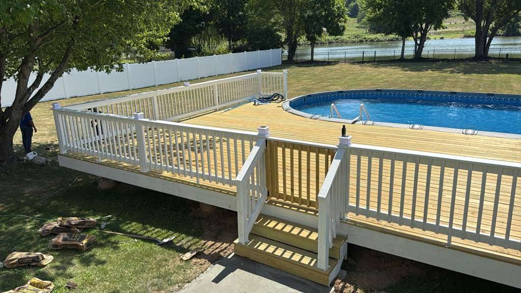 White vinyl privacy fence behind a wood pool deck with white vinyl railing beside an above-ground pool on a waterfront property
